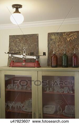 Scales Collection: Red cast iron scale on top of cabinet filled with Candlewick glassware. Antique ceiling tin panels, 3 glass spritzer bottles View Large Photo Image Stock Photo - Scales Collection: Red cast iron scale on top of cabinet filled with Candlewick glassware. Antique ceiling tin panels, 3 glass spritzer bottles. Fotosearch