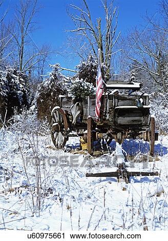 Stock Image - SEASONS; WINTER, Wagon with an American flag left in a field, snow covered, blue skies. Fotosearch