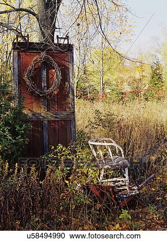 Stock Image - Seasons/Fall: Barn door leaning against tree, wreath, wooden chair. . Fotosearch