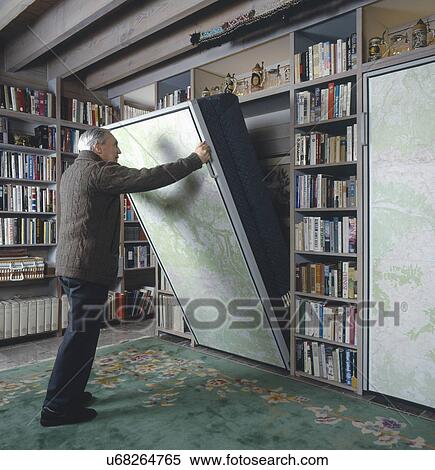 Stock Photography - Senior man pulling Murphy bed in library of a traditional house. Fotosearch