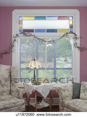 SITTING ROOMS: Family room detail of stained glass window with frosted and colored panes, faux vine, white molding pink walls, soft floral on wing chair and sofa, end table covered in vintage linen, stained glass table lamp, pears on plate View Large Photo Image Stock Image - SITTING ROOMS: Family room detail of stained glass window with frosted and colored panes, faux vine, white molding pink walls, soft floral on wing chair and sofa, end table covered in vintage linen, stained glass table lamp, pears on plate. Fotosearch