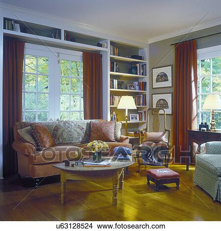 SITTING ROOMS - Traditional with French Country influence, coral couch with pillows, built in book shelves, French doors, red drapes, wood floor. View Large Photo Image Picture - SITTING ROOMS - Traditional with French Country influence, coral couch with pillows, built in book shelves, French doors, red drapes, wood floor.. Fotosearch