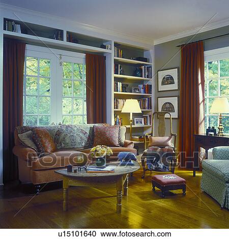 SITTING ROOMS - Traditional with French Country influence, coral couch with pillows, built in book shelves, French doors, red drapes, wood floor. View Large Photo Image Stock Image - SITTING ROOMS - Traditional with French Country influence, coral couch with pillows, built in book shelves, French doors, red drapes, wood floor. . Fotosearch