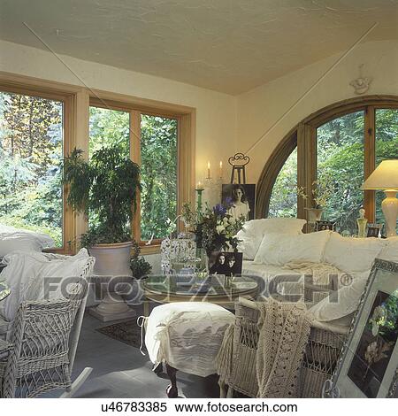 SOLARIUM: Arched window, wicker sofa and chairs, white cushions, glass top coffee table with black and white photographs, cottage romantic style, stucco walls View Large Photo Image Stock Photography - SOLARIUM: Arched window, wicker sofa and chairs, white cushions, glass top coffee table with black and white photographs, cottage romantic style, stucco walls . Fotosearch