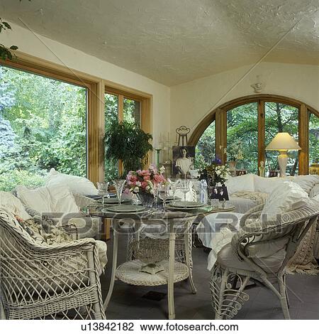 SOLARIUM: White wicker cushions, wicker dining table, set for dinner, pink gerberas, arched window, cottage romantic style, stucco walls and ceiling. View Large Photo Image Stock Image - SOLARIUM: White wicker cushions, wicker dining table, set for dinner, pink gerberas, arched window, cottage romantic style, stucco walls and ceiling.. Fotosearch