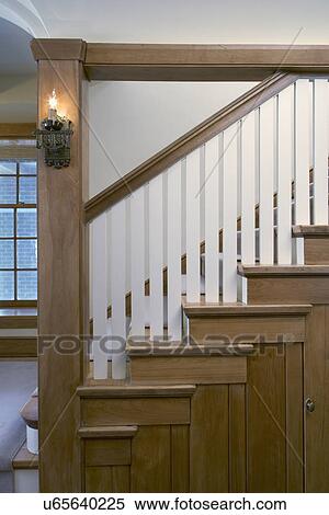 Stock Photography - STAIRWAYS: Arts and crafts style, warm stained wood, balusters are white, sconces on support column, simple and clean lined, side view close up. Fotosearch