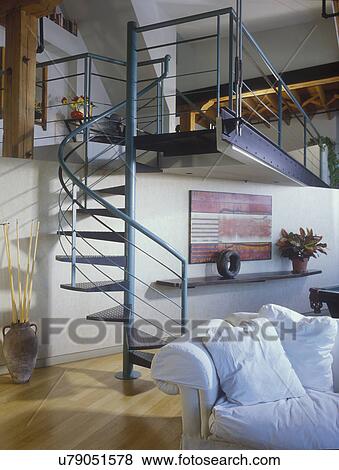 Stock Photo - STAIRWAYS Teal colored metal spiral staircase in a loft, wooden floors, stairs going from living area to bedroom, partial white slip covered sofa, contemporary artwork on wall, suspended shelf . Fotosearch
