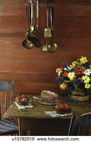 STILL LIFE: Rustic farm table set with a wooden bucket of flowers, strawberries and bread, red barn wood walls, hanging rack of utensils, quiet friendship, simple setting View Large Photo Image Stock Photo - STILL LIFE: Rustic farm table set with a wooden bucket of flowers, strawberries and bread, red barn wood walls, hanging rack of utensils, quiet friendship, simple setting. Fotosearch