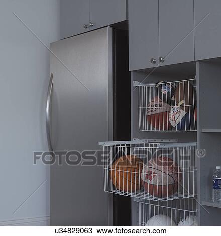 Stock Image - STORAGE: Garage area with stainless steel refrigerator, pullout wire bins hold balls. Fotosearch
