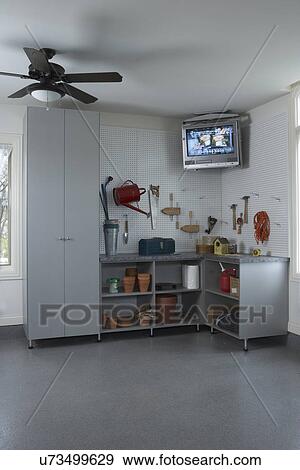 Storage Garage Organization Corner With Tv Suspended Above Peg Board Open Cabinets Store Gardening Tools Closed Cabinet To Left Ceiling Fan