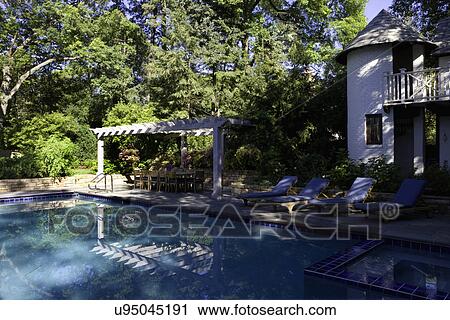 SWIMMING POOLS: French Normandy style two story pool house, four lounge chairs, pergola with dining set, hot tub in right foreground View Large Photo Image Stock Image - SWIMMING POOLS: French Normandy style two story pool house, four lounge chairs, pergola with dining set, hot tub in right foreground. Fotosearch