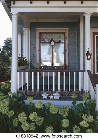 Stock Image - Swing on front porch with hydrangeas growing in garden. Fotosearch