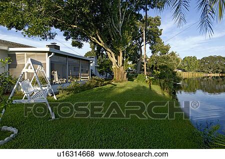 Stock Photo - Swing on grass at the back yard of average home along pond. Fotosearch
