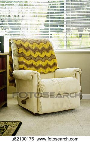 Stock Photograph - Throw blanket on reclining armchair in front of window. Fotosearch