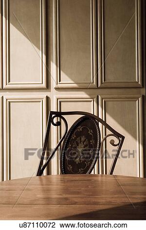 Stock Image - Tipped chair behind wood dining table; Ontario; California; USA. Fotosearch