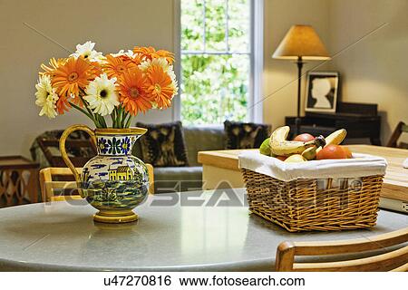 Stock Photograph - Water pitcher with flowers and basket of fruit on countertop. Fotosearch