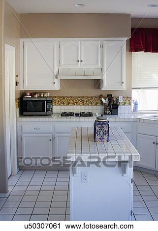 Stock Image - White monochromatic traditional kitchen with island, Laguna Beach, California, USA. Fotosearch