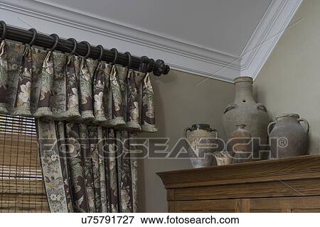 Window treatment with pattern fabric valance and drapery hanging from wooden fluted decorative rod with decorative finial. Bamboo blinds hand from beneath valance and drapery. Pottery displayed in group on top of wooden cabinet. View Large Photo Image Stock Photo - Window treatment with pattern fabric valance and drapery hanging from wooden fluted decorative rod with decorative finial. Bamboo blinds hand from beneath valance and drapery. Pottery displayed in group on top of wooden cabinet.. Fotosearch