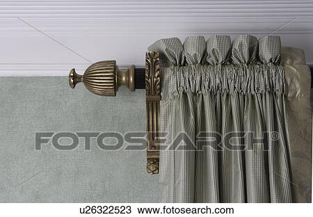 Stock Image - WINDOW TREATMENTS: detail of rod pocket sage green drape with gold curtain rod and finial detail. Fotosearch