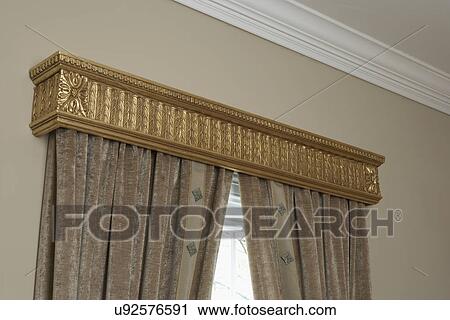 Stock Image - WINDOW TREATMENTS: gold cornice above silk drapes, beige wall, white crown molding. Fotosearch