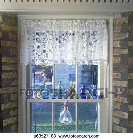 Stock Photo - WINDOW TREATMENTS: Window in brick wall of Great Room, colored bottle collection, on window sill, brick walls, lace valance. . Fotosearch