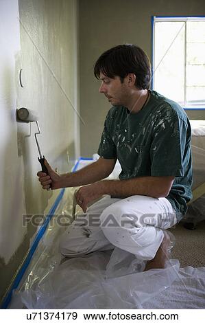 Stock Photo - Young man with paint roller painting a room. Fotosearch