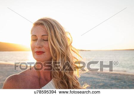 Blond woman with eyes closed on beach at dusk, Cape Town, South Africa View Large Photo Image Picture - Blond woman with eyes closed on beach at dusk, Cape Town, South Africa. Fotosearch
