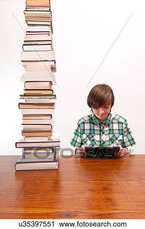 Boy at desk with tall stack of books and digital tablet View Large Photo Image Stock Image - Boy at desk with tall stack of books and digital tablet. Fotosearch