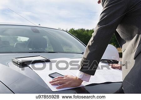 Stock Photo - Businessman checking blueprint on car bonnet. Fotosearch