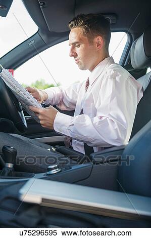 Stock Photography - Businessman in car looking at paperwork. Fotosearch