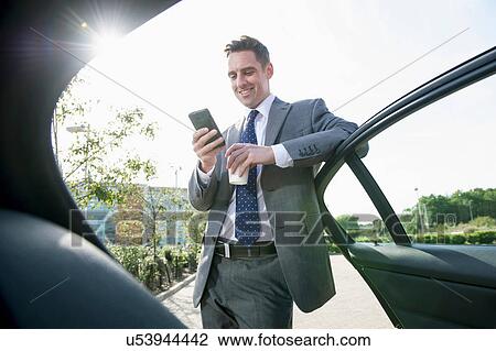 Businessman leaning against car door using smartphone View Large Photo Image Stock Image - Businessman leaning against car door using smartphone. Fotosearch