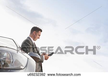Businessman looking at digital tablet whilst leaning against car View Large Photo Image Stock Image - Businessman looking at digital tablet whilst leaning against car. Fotosearch