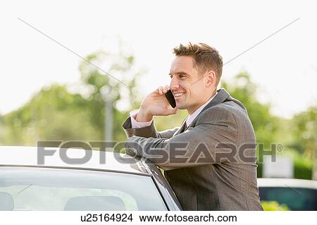 Businessman talking on mobile whilst leaning against car View Large Photo Image Picture - Businessman talking on mobile whilst leaning against car. Fotosearch