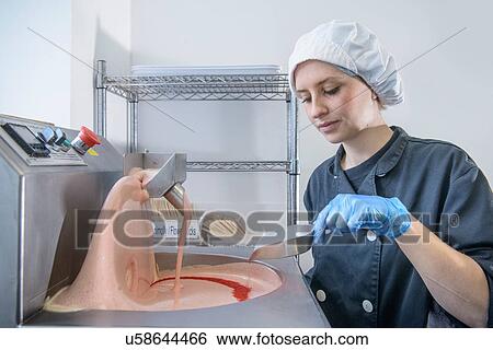 Stock Photograph - Chocolatier adding ingredients to machine in sweet factory. Fotosearch