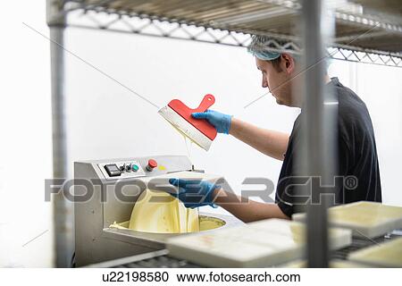 Stock Image - Chocolatier smoothing white chocolate in sweet factory. Fotosearch