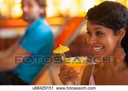 Stock Image - Close up of young woman holding cocktail at indoor beach party. Fotosearch