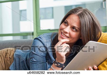 Stock Image - Close up of young woman lying on sofa holding digital tablet. Fotosearch