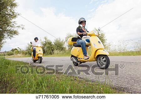 Couple on scooters riding down rural road View Large Photo Image Stock Photography - Couple on scooters riding down rural road. Fotosearch