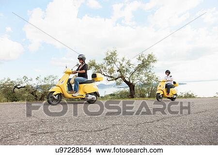 Picture - Couple on scooters riding up rural road. Fotosearch