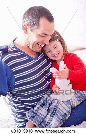Stock Image - Father and young daughter sitting on bed. Fotosearch