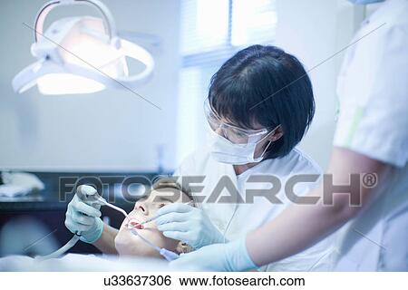 Stock Photograph - Female dentist checking patients teeth. Fotosearch