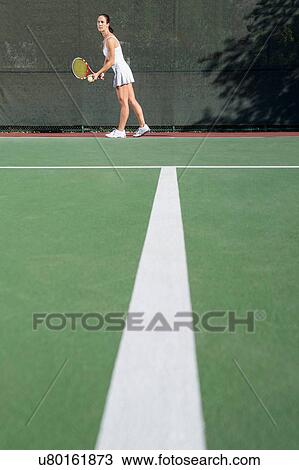Stock Image - Female tennis player on court preparing to serve. Fotosearch