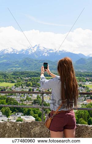 Stock Image - Female tourist photographing view of Alps, Salzburg, Austria. Fotosearch
