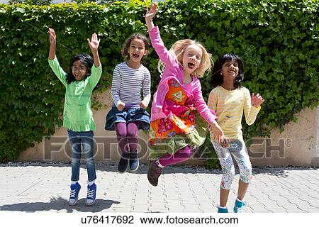 Stock Image - Four girls jumping in garden. Fotosearch