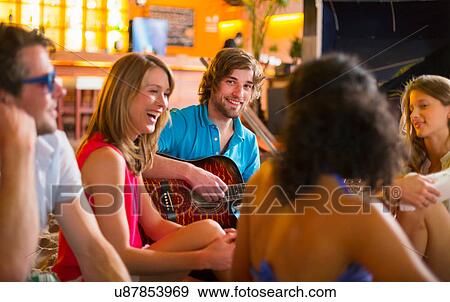 Stock Photo - Friends enjoying guitar playing in bar. Fotosearch
