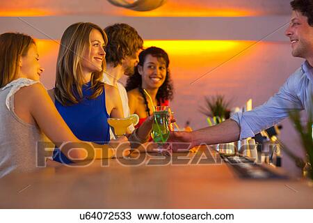 Stock Image - Group of friends ordering cocktails in bar. Fotosearch