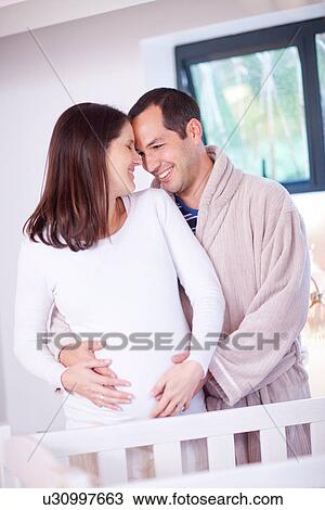 Stock Image - Husband and wife hugging baby bump. Fotosearch