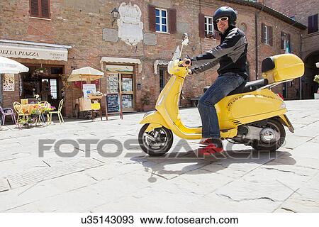 Stock Image - Man on scooter in village square. Fotosearch