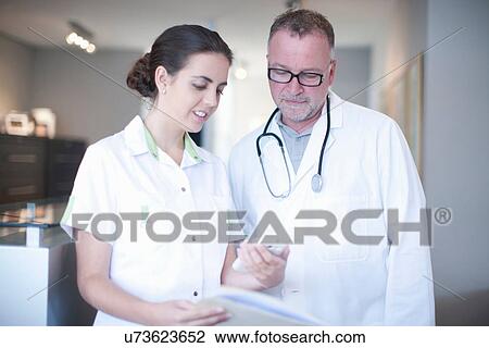 Stock Image - Nurse and doctor looking at mobile in hospital reception. Fotosearch