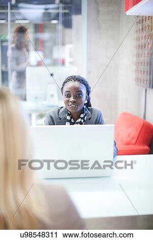 Stock Image - Office workers chatting at desk. Fotosearch